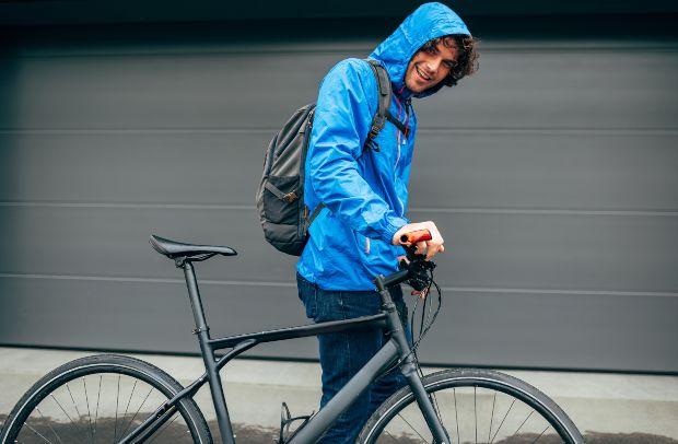 Junger Mann mit Fahrrad, mit Regenjacke bekleidet