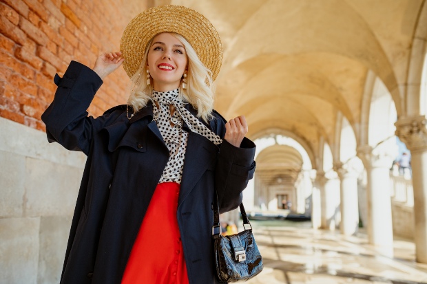 Junge stylische frau mit Strohhut, Polka-Bluse, rotem Rock und schwarzem Mantel - Blusen für den Herbst