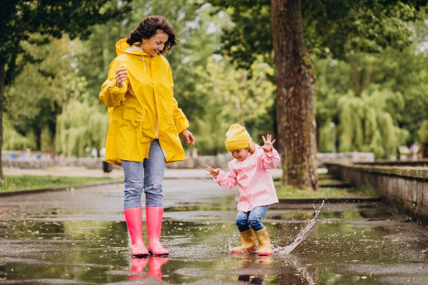Mutter mit Kind in Regenkleidung spielt in Pfützen - Regenmode