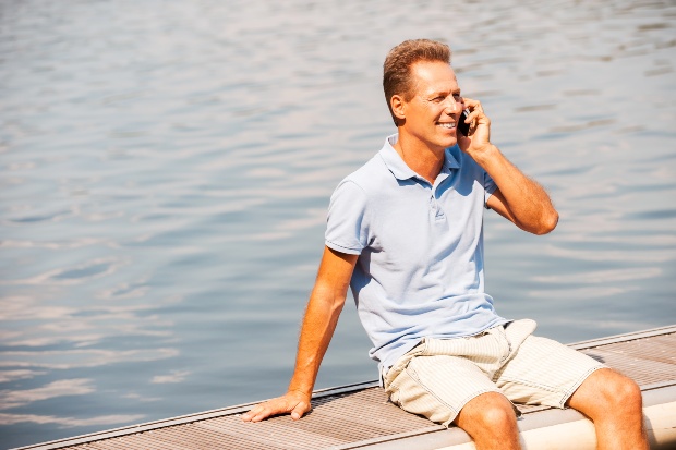 Mann-Poloshirt-sitzt-am-Wasser-und-telefoniert