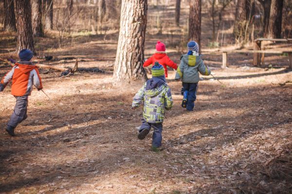 Kinder spielen im Wald. Alle mit Mütze und Jacke ausgestattet