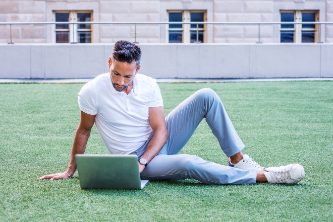 Mann-mit-weissem-Polo-Shirt-auf-Rasen-mit-Laptop - Weißes Poloshirt für Herren