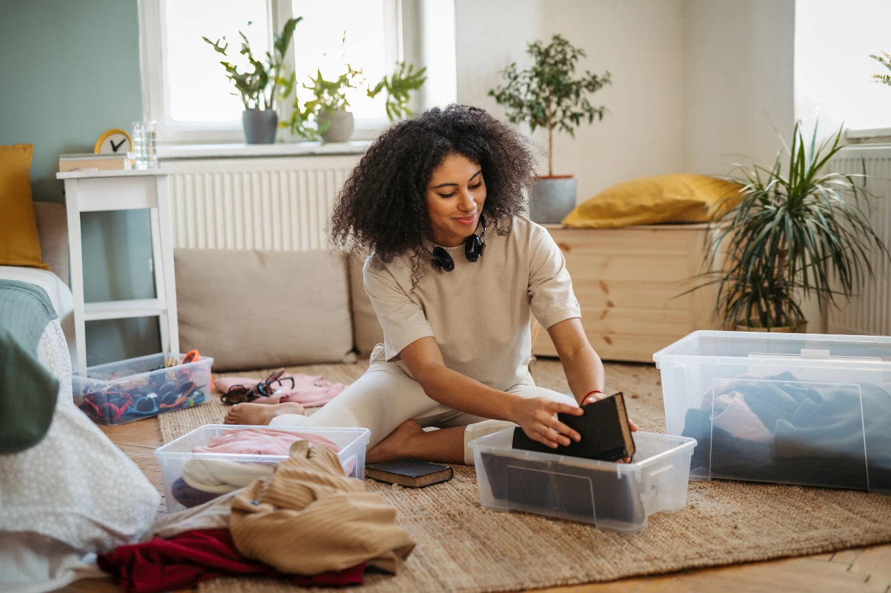Frau sitzt auf dem Boden und sortiert Accessoires und Kleidung in transparente Boxen
