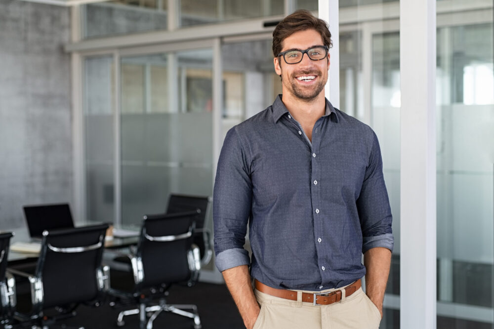 Business Casual erlaubt mehr Freiheit bei der Kleiderwahl, ohne auf Seriosität zu verzichten Mann in lockerem, seriösem Hemd und hellen Chino-Hosen vor Bürokulisse - Business Dresscode - Was ziehe ich an im Büro?