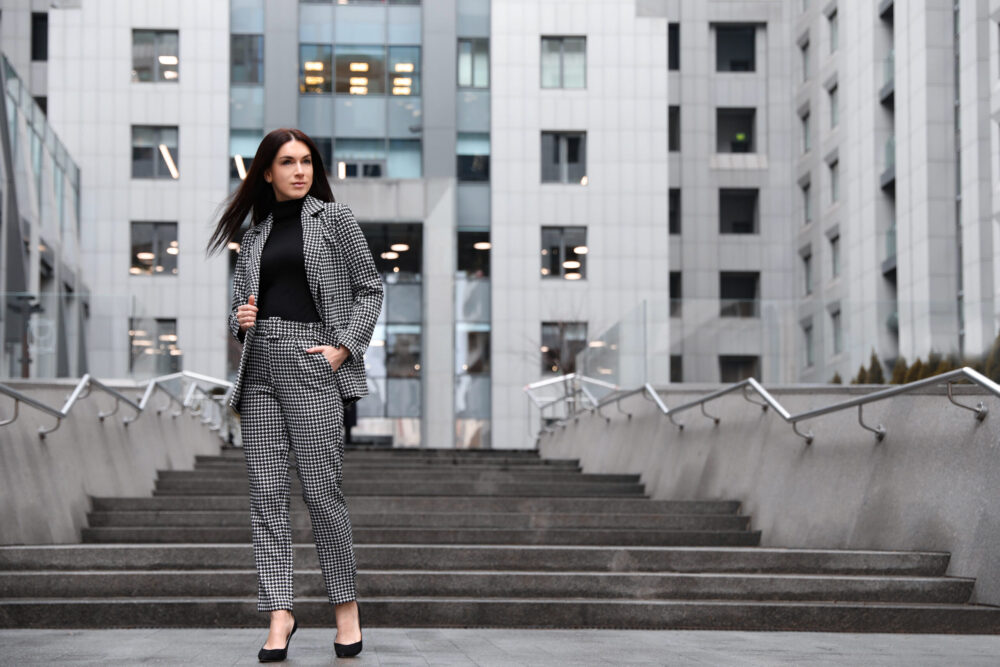 Ein Hosenanzug für Damen ist mehr als ein Klassiker – er ist ein Statement für Stil und Kompetenz Portrait von Frau in Hosenanzug vor Betontreppe und Hochhauskulisse - Business Dresscode - Was ziehe ich an im Büro?