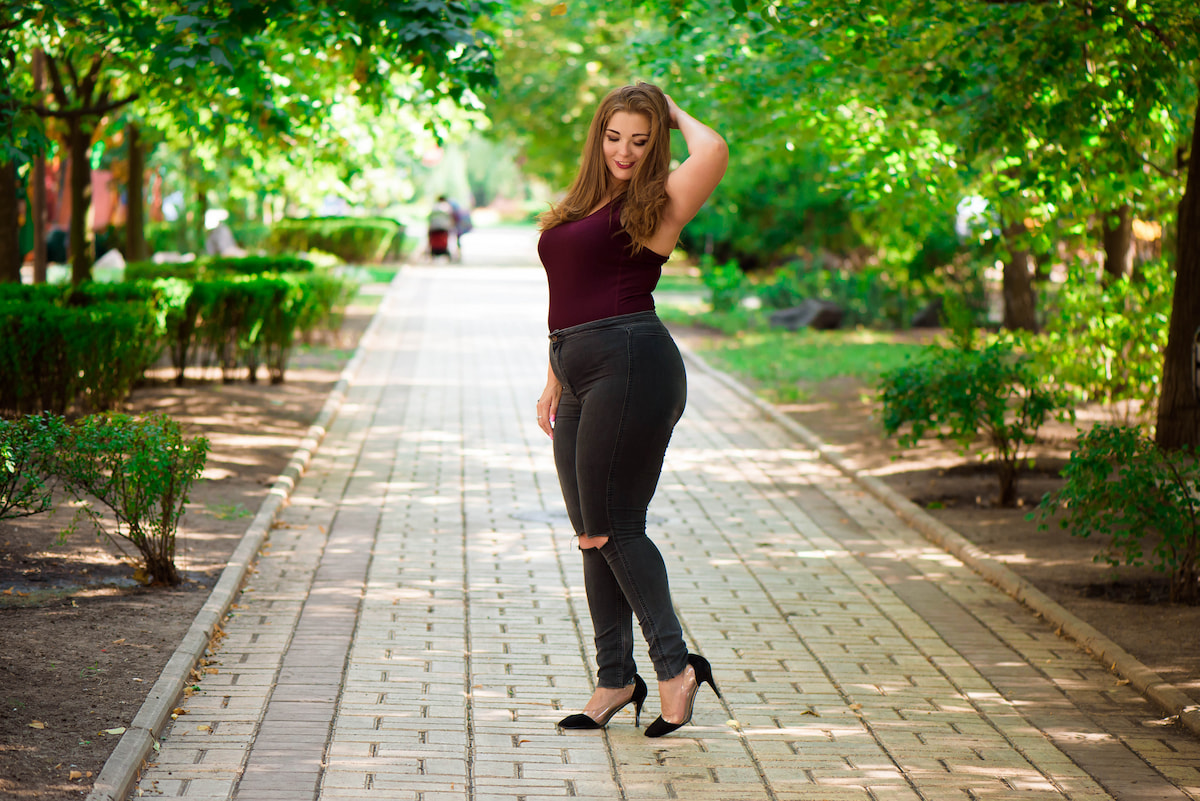 Eine Drittelaufteilung macht nicht nur Curvy-Outfits attraktiver und kann den Fokus von Problemzonen ziehen. Hunge Frau mit schwarzen Jeans, dunkelrotem Top und Absatzschuhen im Park