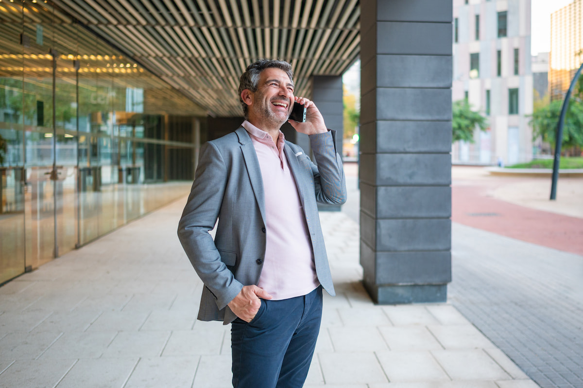 Mann in Casual Anzug mit pinkem Poloshirt telefoniert und lacht dabei